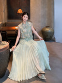 Sitting model in a sage green pleated skirt with a matching embroidered top, highlighting the elegant pleats and comfortable fit.