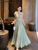 Front view of a sage green pleated maxi skirt paired with a matching top and white handbag, crafted from a breathable Lyocell-Polyester blend.