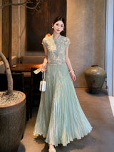 Front view of a sage green pleated maxi skirt paired with a matching top and white handbag, crafted from a breathable Lyocell-Polyester blend.