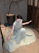 Sitting model on the floor in a sage green pleated skirt and embroidered top, showcasing the full, flowing skirt and delicate details.