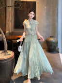 Model in a sage green pleated maxi skirt with a matching top, holding a fan and white bag, styled for a refined New Chinese look.