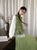 Seated styling of a sage green Songjin silk rabbit vest paired with a soft pleated skirt.
