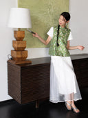 Model wearing a sage green rabbit-print Songjin silk vest over a white blouse and flowing white skirt.
