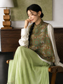 Model wearing a sage green dragon and phoenix Songjin silk vest with a soft pleated skirt in a seated pose.