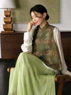Model wearing a sage green dragon and phoenix Songjin silk vest with a soft pleated skirt in a seated pose.