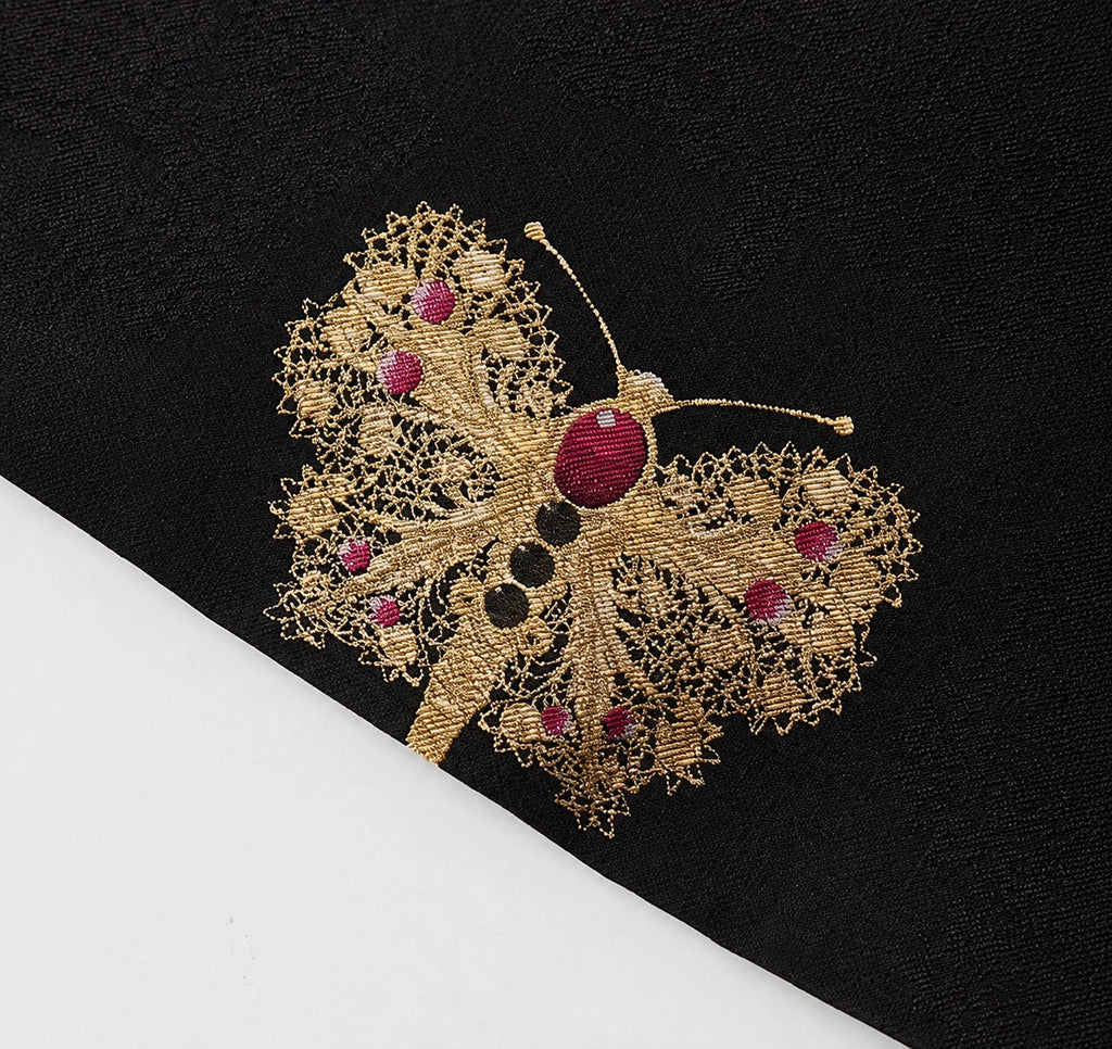 Close-up of an intricately woven gold and magenta butterfly motif on black silk brocade