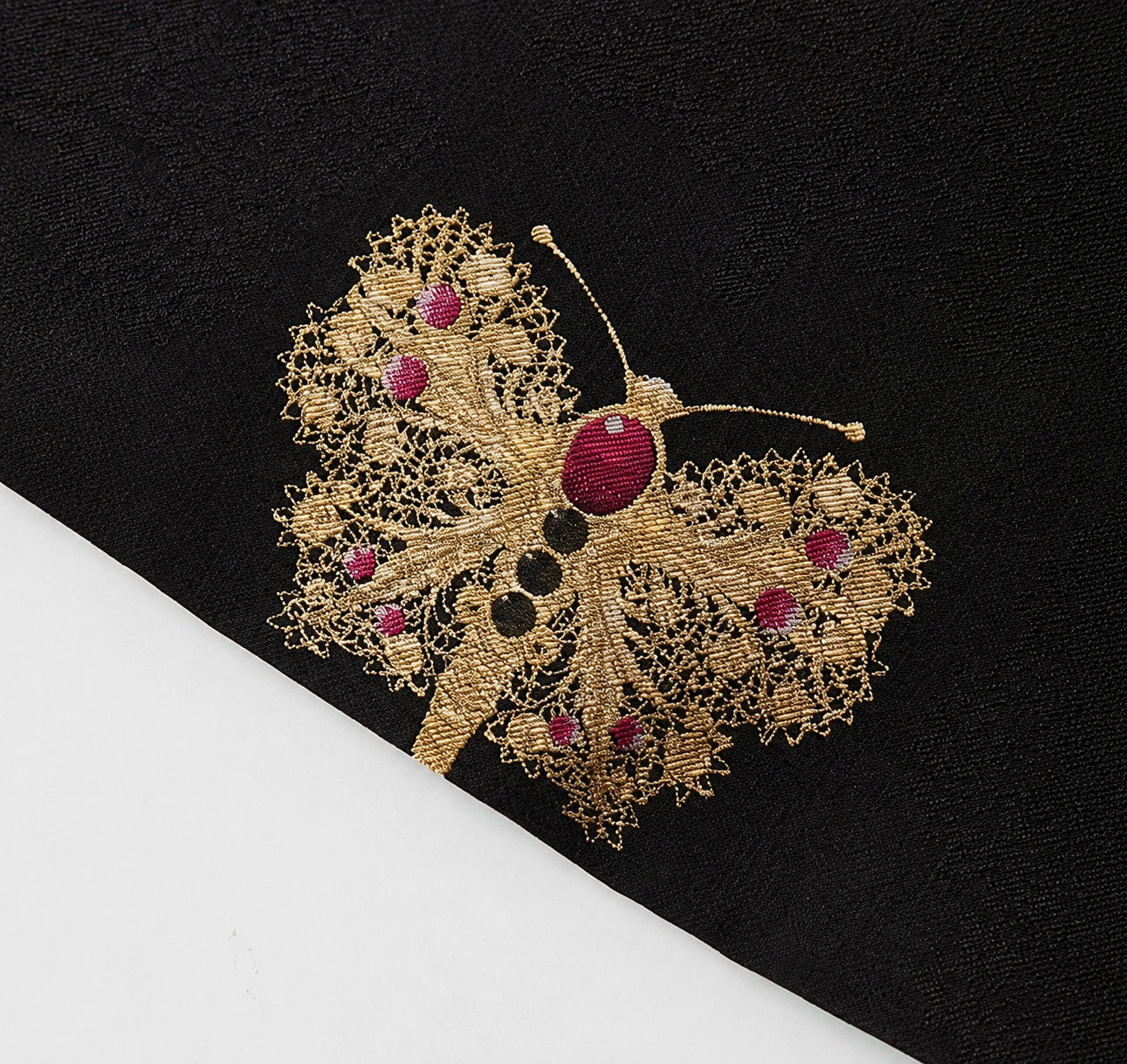 Close-up of an intricately woven gold and magenta butterfly motif on black silk brocade