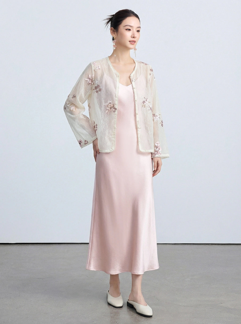 Full-body shot of a light beige sheer cardigan with pearl-trimmed edges and intricate embroidery, styled with a pink satin slip dress.