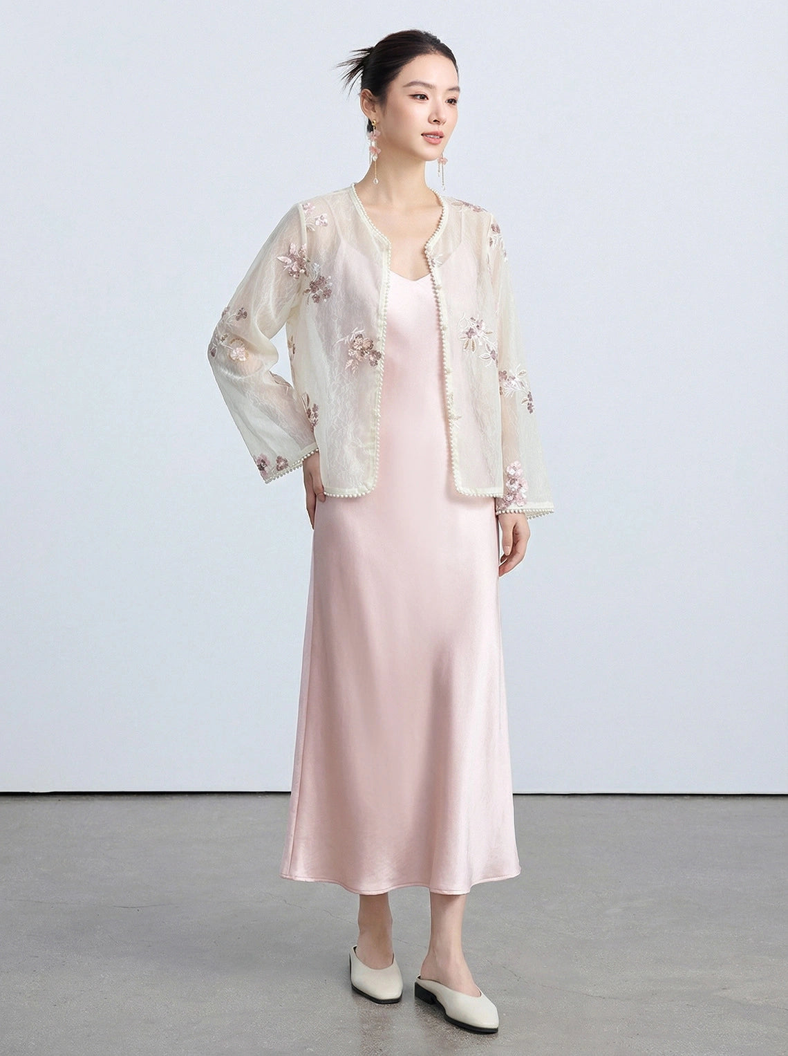 Full-body shot of a light beige sheer cardigan with pearl-trimmed edges and intricate embroidery, styled with a pink satin slip dress.