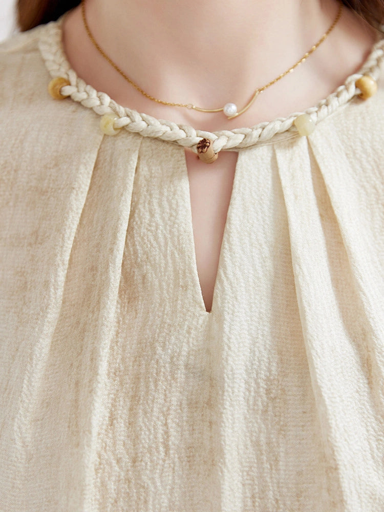 Close-up detail of a mulberry silk blouse featuring a braided neckline with decorative beads and a delicate keyhole opening.