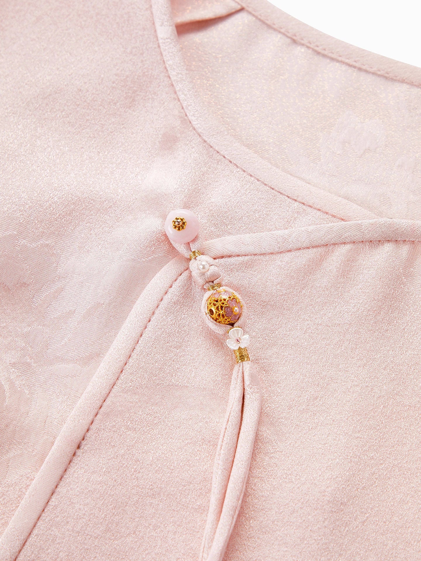 Close-up of the diagonal placket on a pink silk blouse, featuring intricate beadwork, decorative tassels, and a traditional Chinese knot design.
