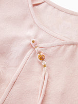 Close-up of the diagonal placket on a pink silk blouse, featuring intricate beadwork, decorative tassels, and a traditional Chinese knot design.
