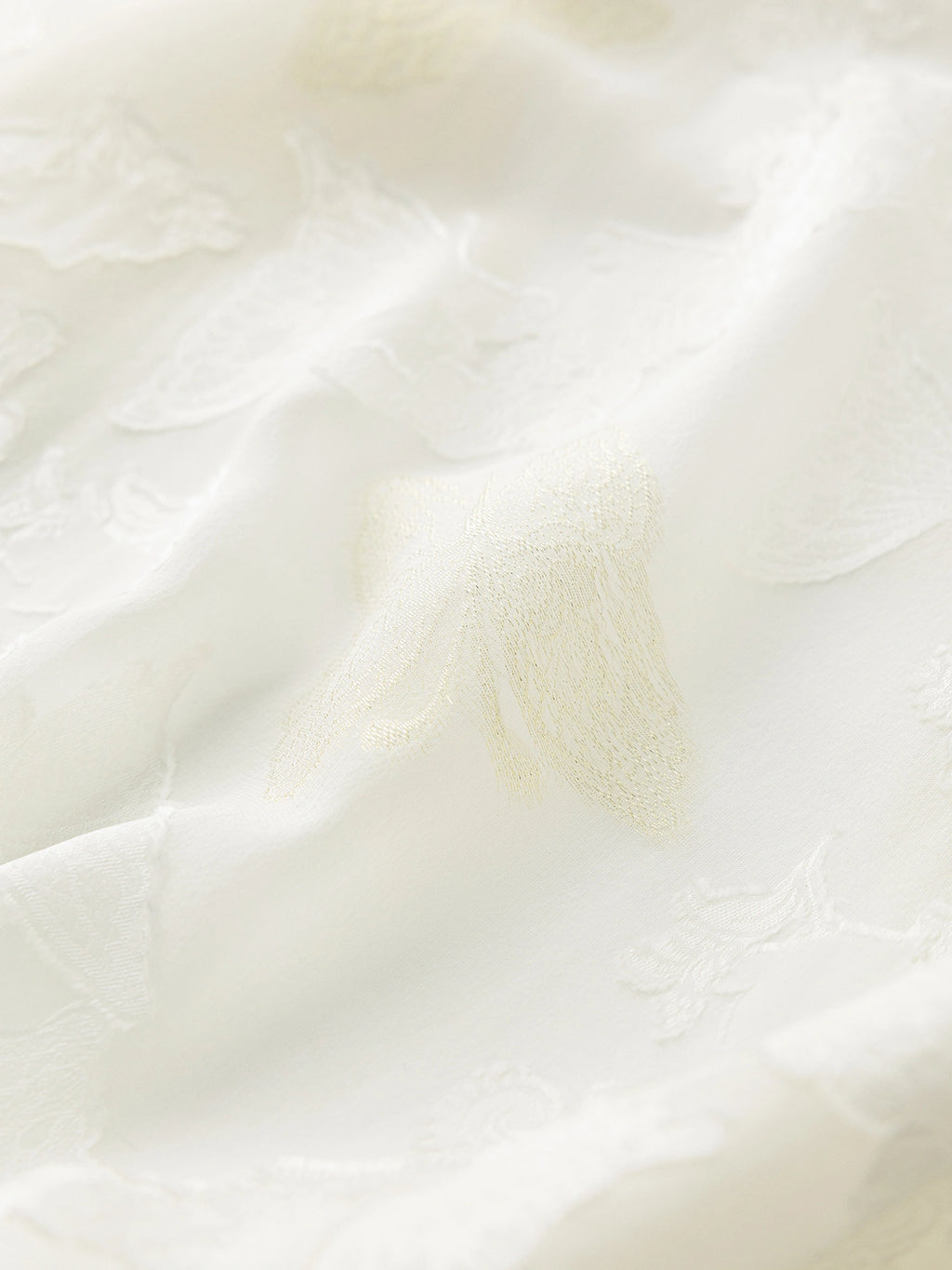 Close-up of the delicate butterfly cutwork embroidery on a white sheer silk top, highlighting the fine craftsmanship and fabric texture.