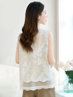 Back view of a white silk vest featuring intricate butterfly cutwork embroidery and a scalloped lace hem, paired with beige trousers.