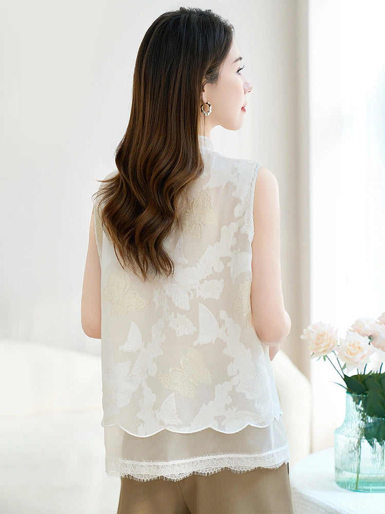 Back view of a white silk vest featuring intricate butterfly cutwork embroidery and a scalloped lace hem, paired with beige trousers.
