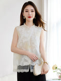 Model wearing a white sleeveless 100% silk vest with a stand collar and sheer cutwork butterfly patterns, paired with a black skirt and holding a pleated bag.