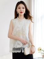 Model wearing a white sleeveless 100% silk vest with a stand collar and sheer cutwork butterfly patterns, paired with a black skirt and holding a pleated bag.
