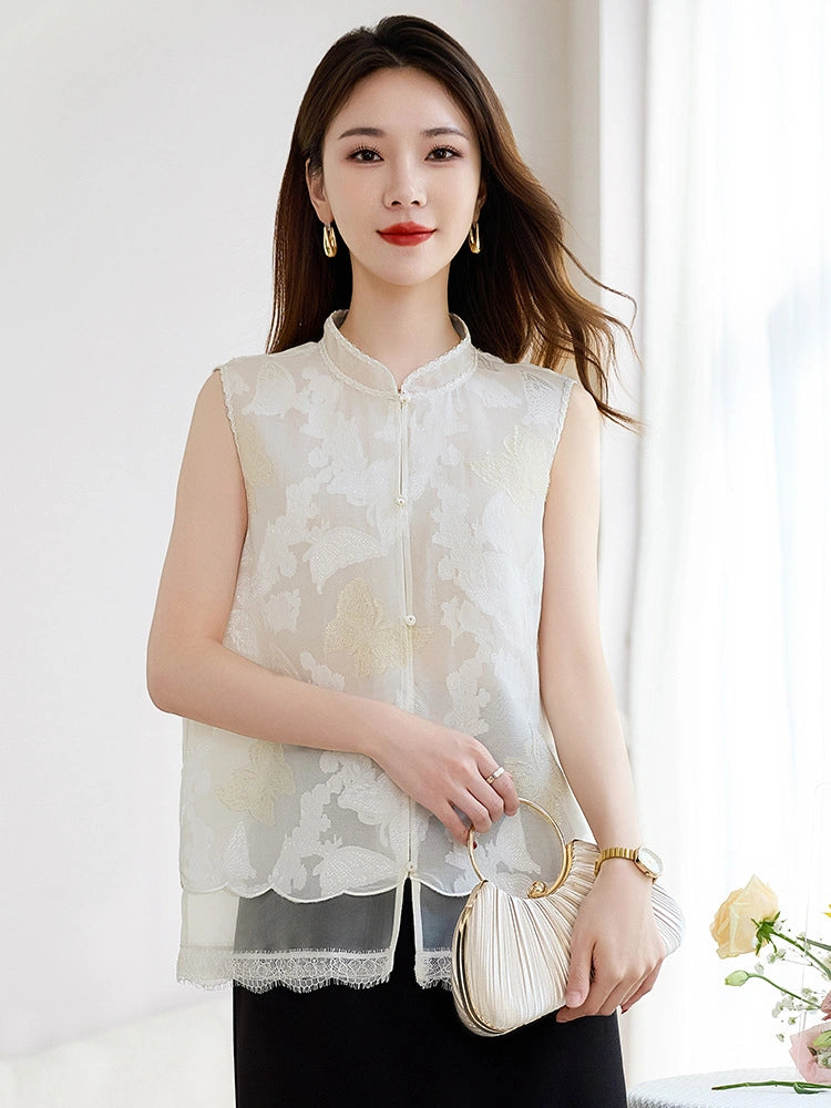 Model wearing a white sleeveless 100% silk vest with a stand collar and sheer cutwork butterfly patterns, paired with a black skirt and holding a pleated bag.