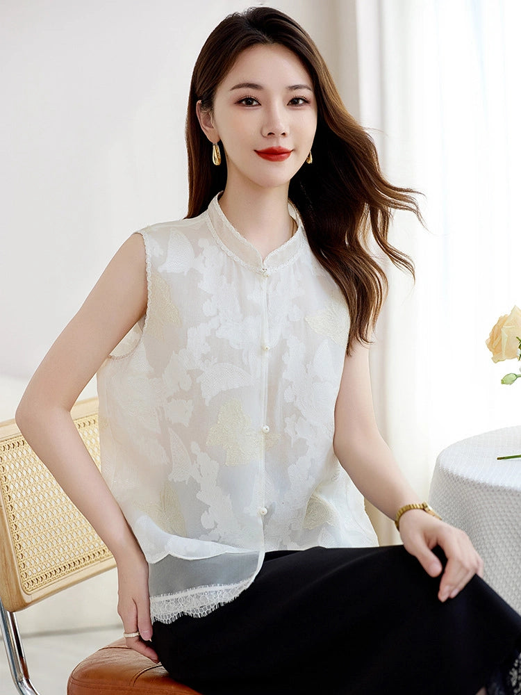 Front view of a woman sitting in a white silk cutwork vest with lace trim and pearl buttons, showcasing the relaxed fit and sheer airy texture.