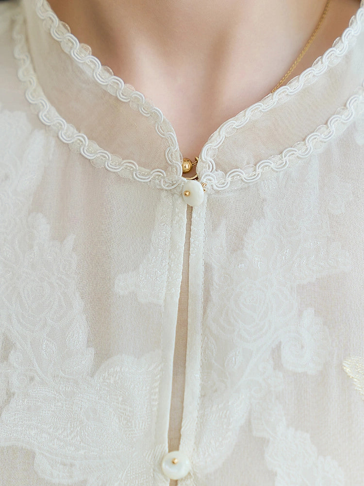 Close-up of a white sheer silk vest featuring a scalloped lace neckline, delicate pearl buttons, and intricate floral cutwork embroidery.