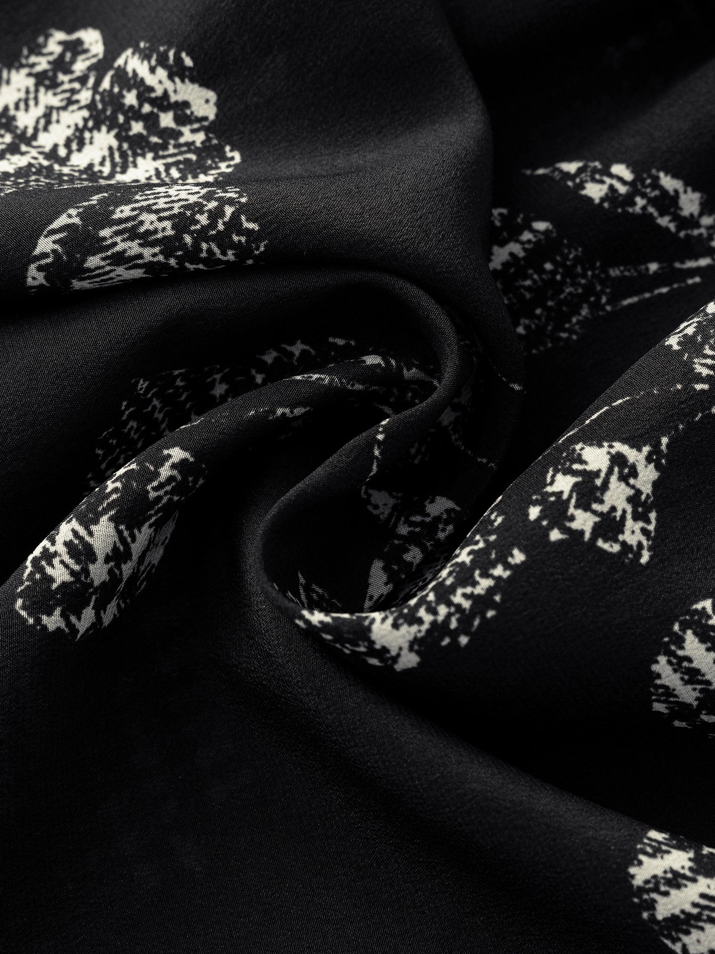 Close-up of the 100% silk crepe fabric showing the crisp white abstract floral print on a black background, highlighting the texture and sheen.