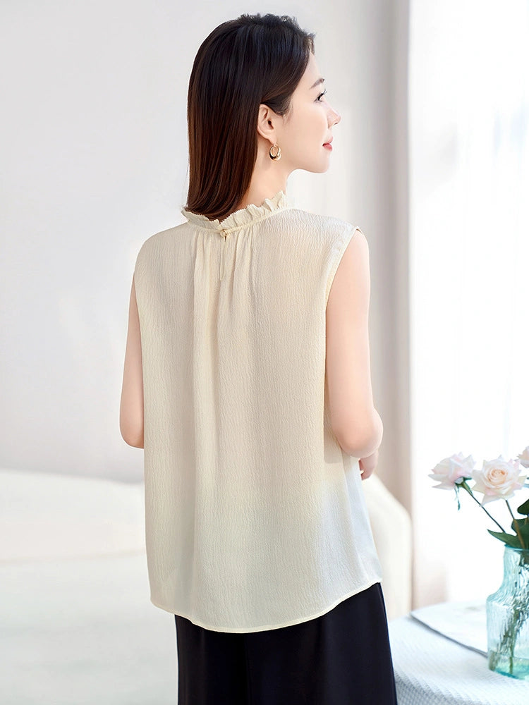 Back view of a cream beige 100% silk sleeveless top with a ruffled neckline and relaxed flowy fit, paired with a black skirt.