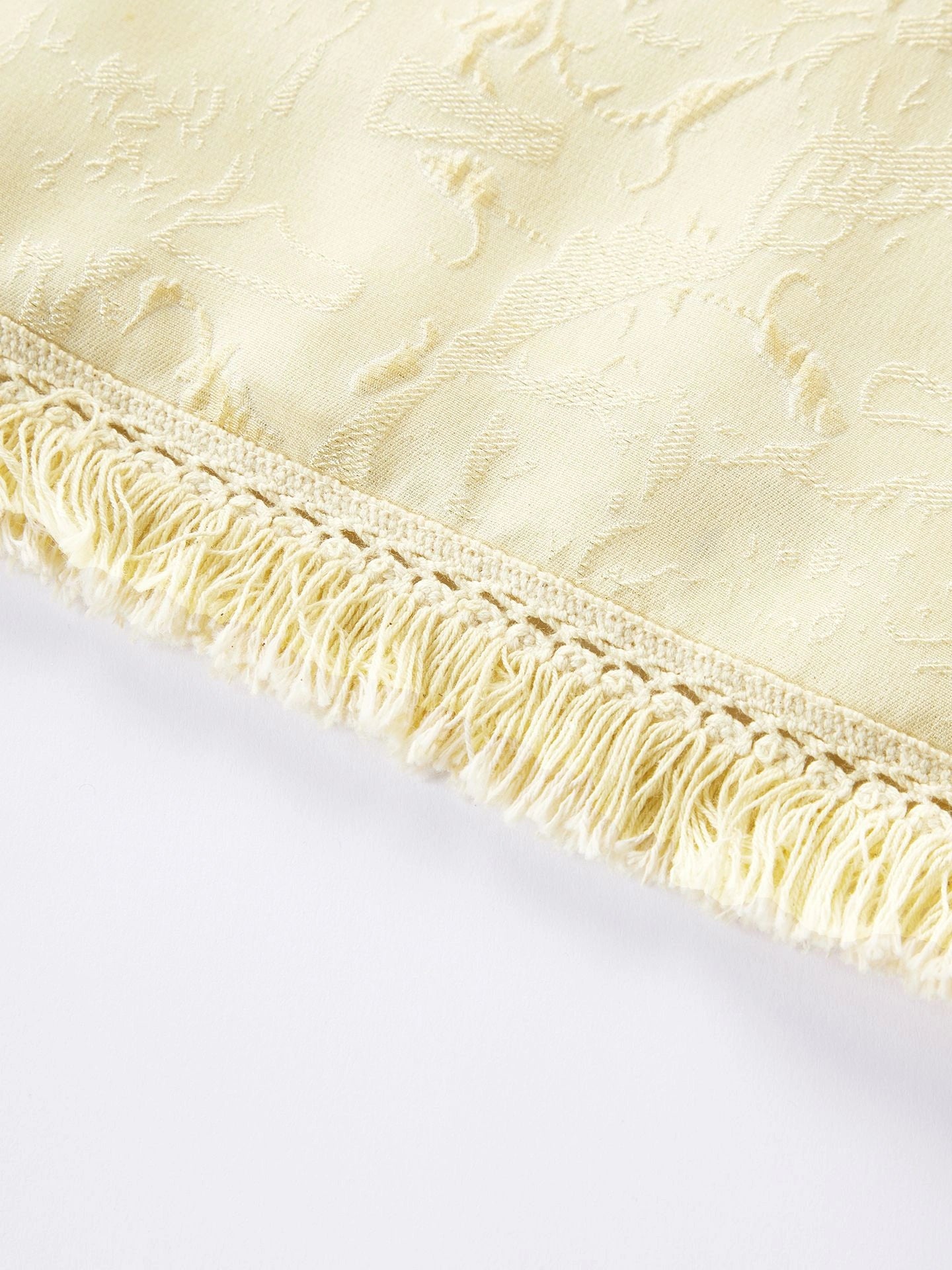 Close-up of the textured jacquard fabric and delicate fringe tassel hem on a cream yellow silk blouse.