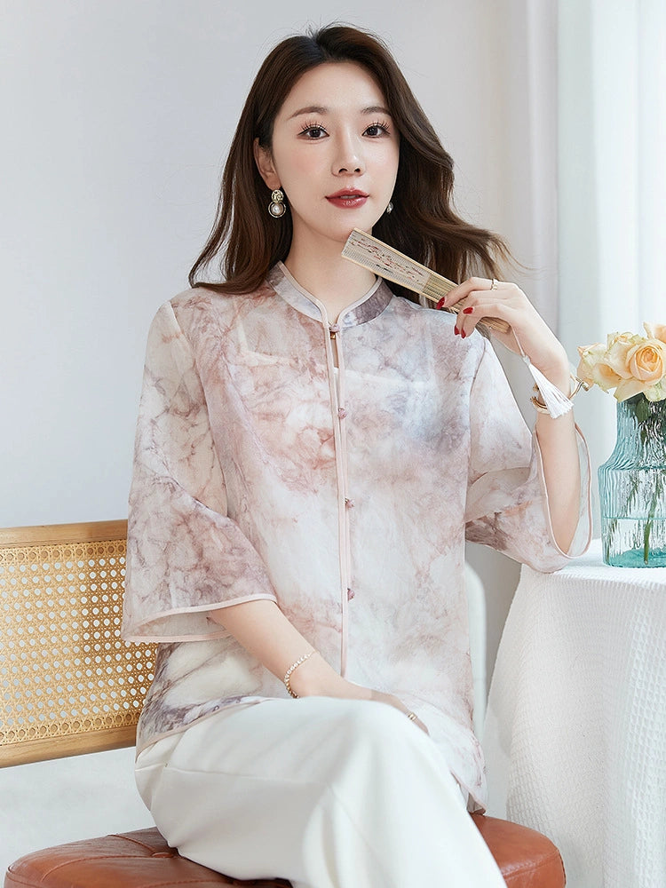 Model seated in a 100% silk New Chinese style top with a stand collar and three-quarter sleeves, holding a fan, highlighting the elegant drape and exquisite print.