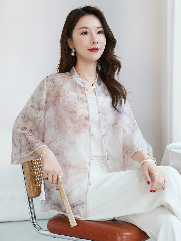Sitting model wearing a 100% silk open-front top with a stand collar, holding a fan, showcasing the lightweight, breathable fabric and relaxed silhouette.