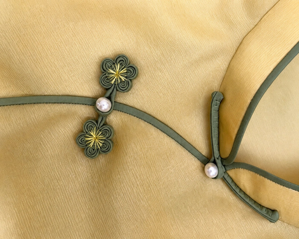 Detail of the flower-shaped frog closures, pearl-style buttons and contrasting piping at the neckline