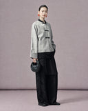 Angled view of a silver-grey floral jacquard Chinese jacket styled with black wide-leg trousers