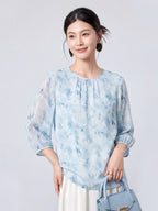 Woman wearing a sky blue printed mulberry silk blouse with a round neck and three-quarter sleeves