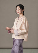 Model wearing the blush jacket with a violet patterned skirt, angled view