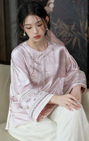 Seated model wearing the smoky pink jacket, with the floral embroidery on both cuffs visible.