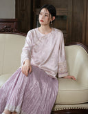 Front view of a seated model wearing the smoky pink jacket with a coordinating pleated skirt.
