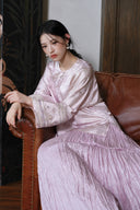 Seated model wearing the smoky pink jacquard jacket and pleated skirt, with one embroidered cuff in view.