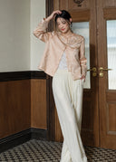 Full-length model look showing the soft peach pink embroidered jacket styled with ivory wide-leg trousers.