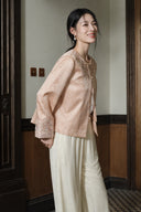 Side view of a model wearing the soft peach pink jacket with embroidered cuffs and ivory wide-leg trousers.
