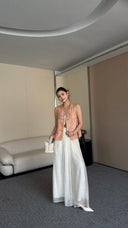 Woman wearing a sleeveless vintage Cheongsam vest top with pink and gold brocade floral pattern, paired with white wide-leg pants and white bag.