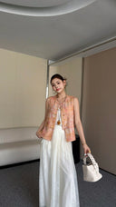 Full body shot of a New Chinese style sleeveless qipao top in soft pink-orange hues, paired with flowy white pants and white pointed heels.