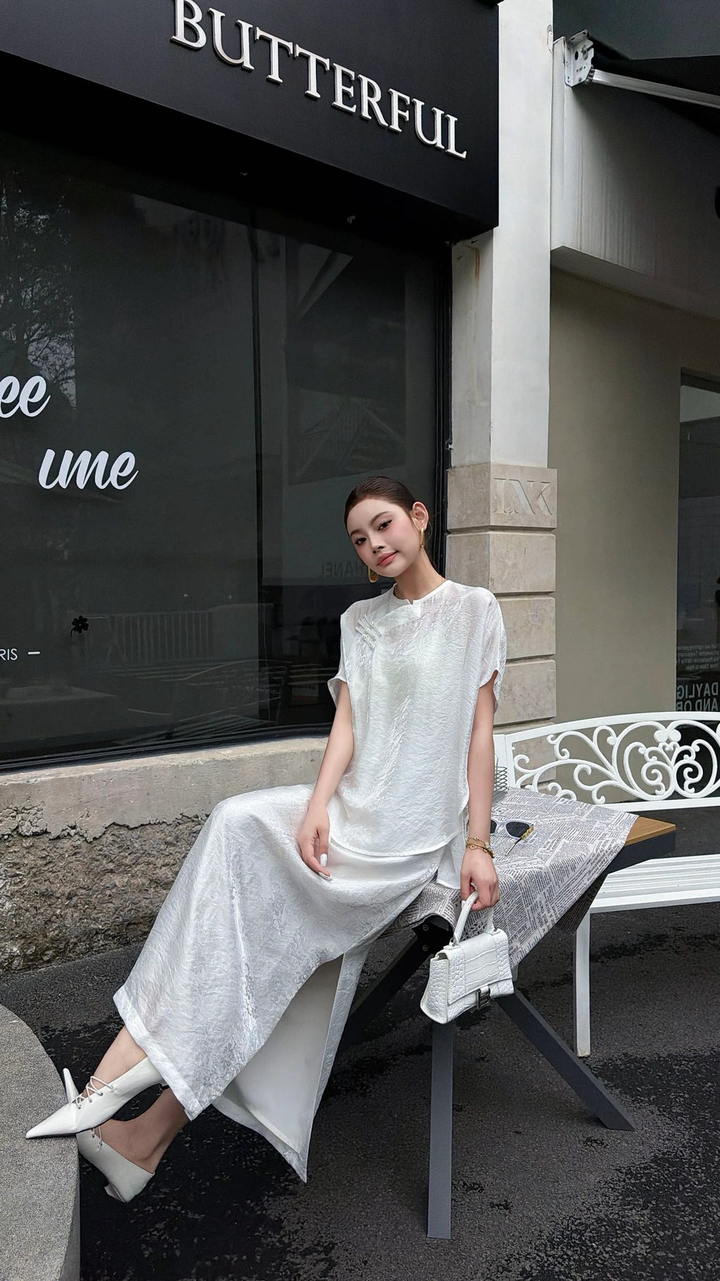 Sitting woman wearing a white short sleeve Cheongsam top and matching midi skirt, showcasing the relaxed fit and elegant drape of the viscose blend fabric.