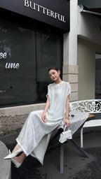 Sitting woman wearing a white short sleeve Cheongsam top and matching midi skirt, showcasing the relaxed fit and elegant drape of the viscose blend fabric.