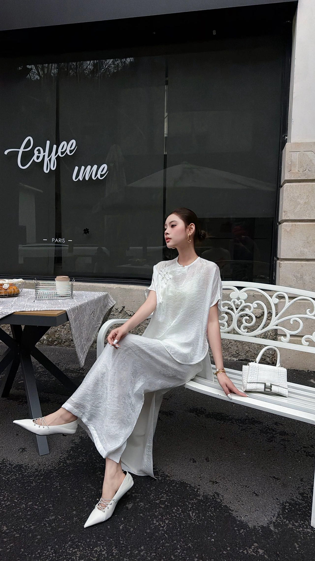 Model sitting on a white bench in a white New Chinese style co-ord set, highlighting the side slit detail on the skirt and the breathable fabric.