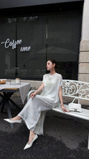 Model sitting on a white bench in a white New Chinese style co-ord set, highlighting the side slit detail on the skirt and the breathable fabric.
