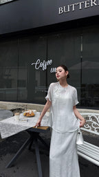 Full body shot of a white Cheongsam blouse and maxi skirt set, featuring a mandarin collar and buttoned front, paired with white heels and a white bag.