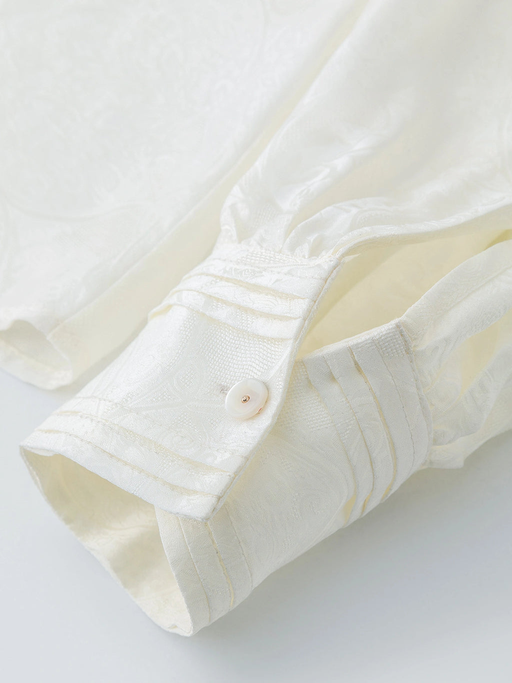 Close-up of the cuff detail on a white jacquard blouse, showing the fine stitching and button finish, crafted from a premium Viscose-Silk blend.