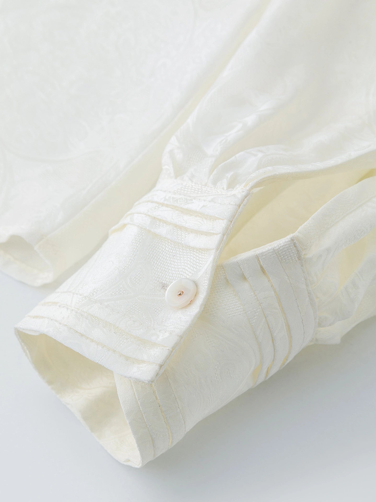 Close-up of the cuff detail on a white jacquard blouse, showing the fine stitching and button finish, crafted from a premium Viscose-Silk blend.