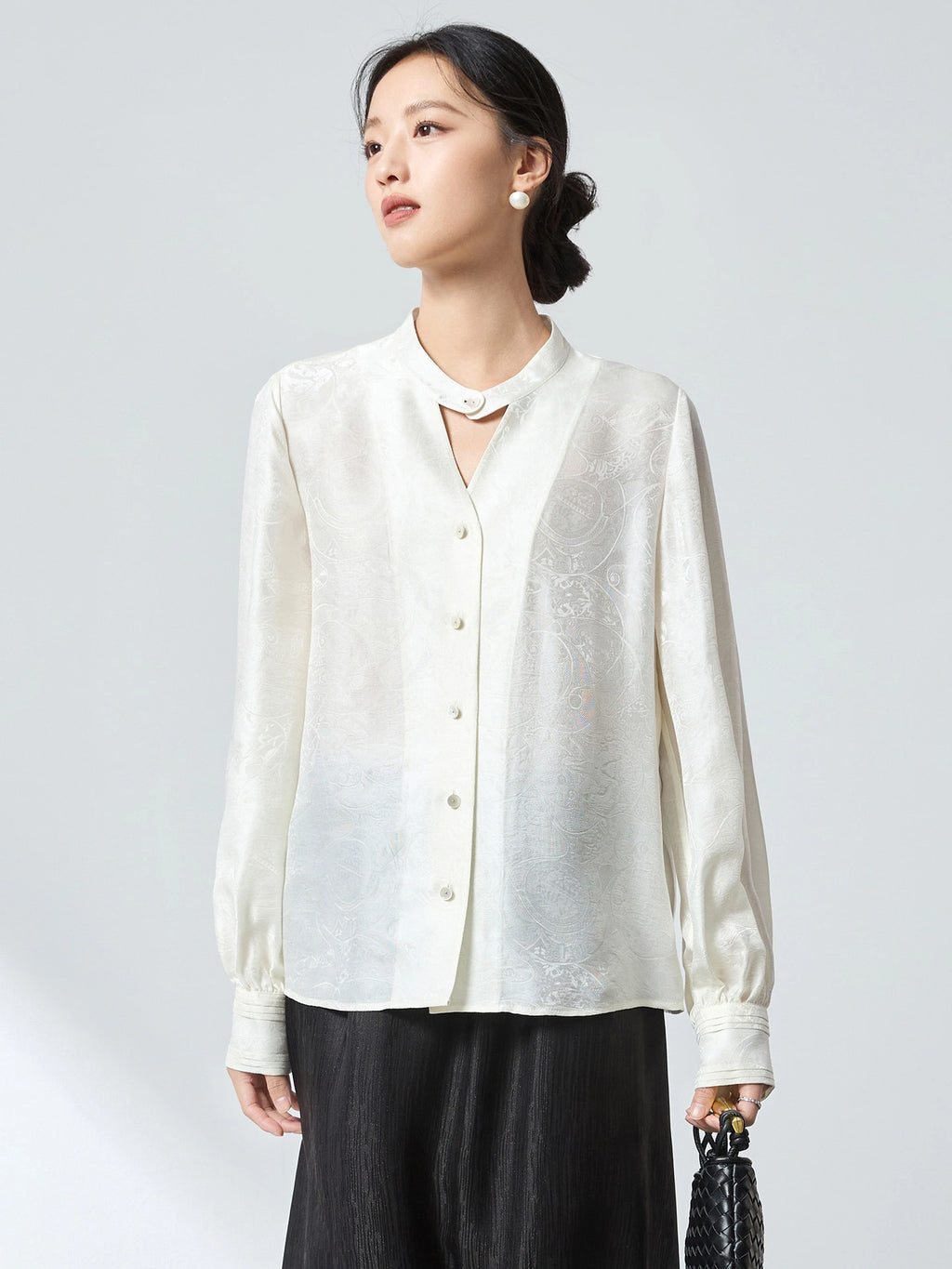 Front view of a white stand-collar blouse with button-down front and delicate jacquard pattern, paired with a black skirt, crafted from 75.2% Viscose and 24.8% Mulberry Silk.