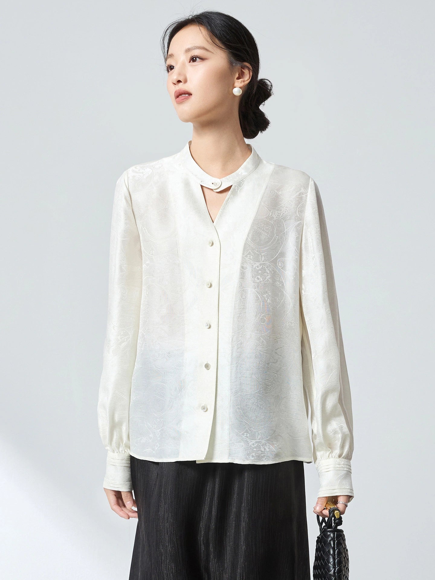 Front view of a white stand-collar blouse with button-down front and delicate jacquard pattern, paired with a black skirt, crafted from 75.2% Viscose and 24.8% Mulberry Silk.