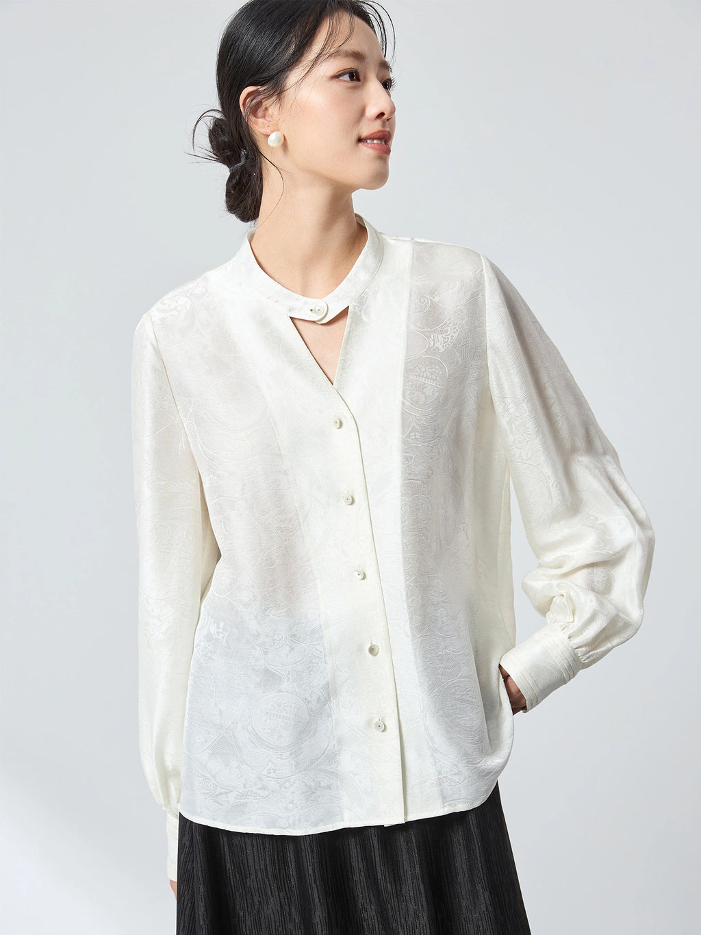 Model wearing a white long-sleeve jacquard blouse with a stand collar, featuring a relaxed fit and subtle floral pattern, perfect for a refined New Chinese look.